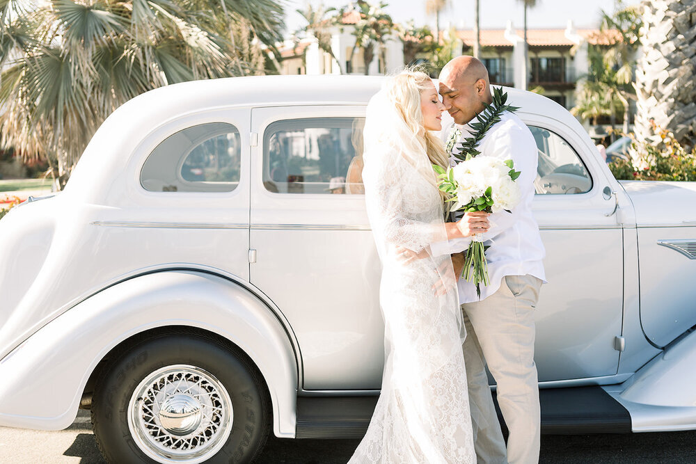  bride and groom kiss in front of vintage getaway car after wedding 