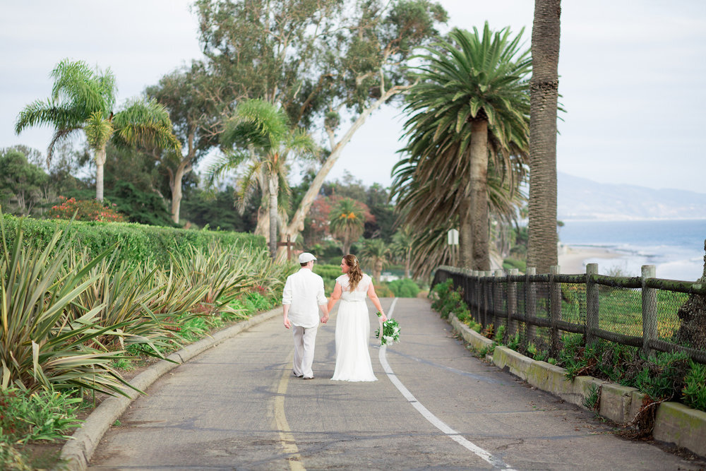  wedding couple walk hand in hand along beach road 