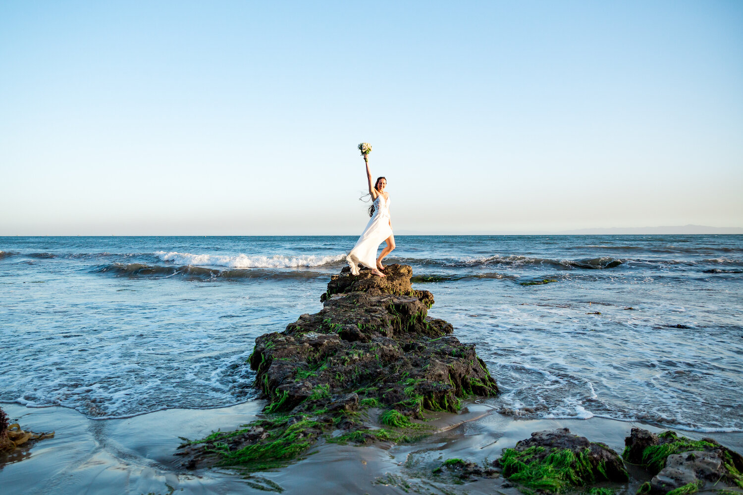  bride with bouquet posed on rock formation on the beach 