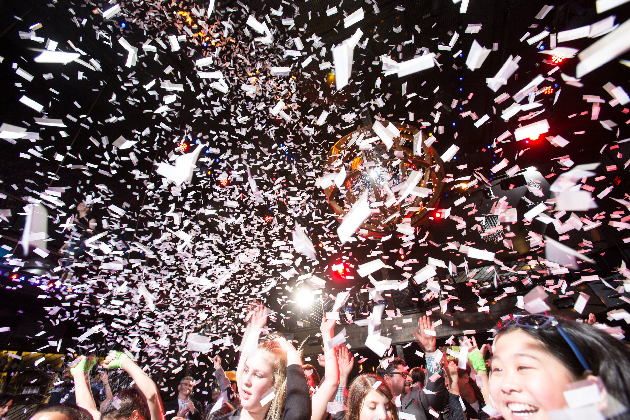 People celebrating in a nightclub with confetti falling and colorful lights.
