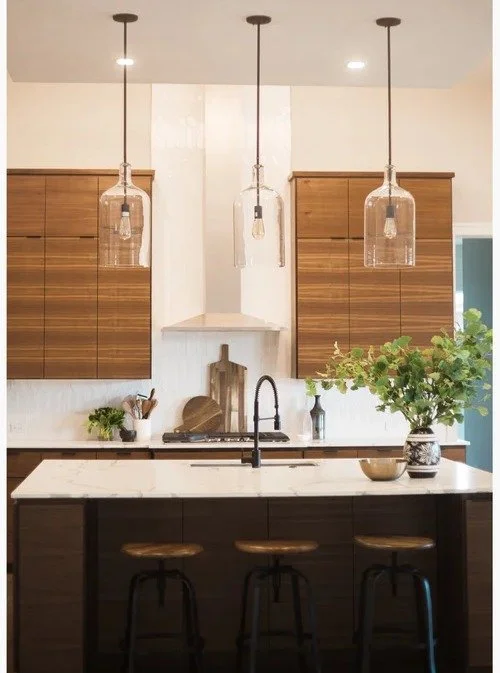 This kitchen is proof that warm wood will never go out of style. 🤎

We designed this space to feel modern, clean, and inviting&mdash;layering rich walnut cabinetry with soft marble veining and sculptural glass pendants for just the right amount of c