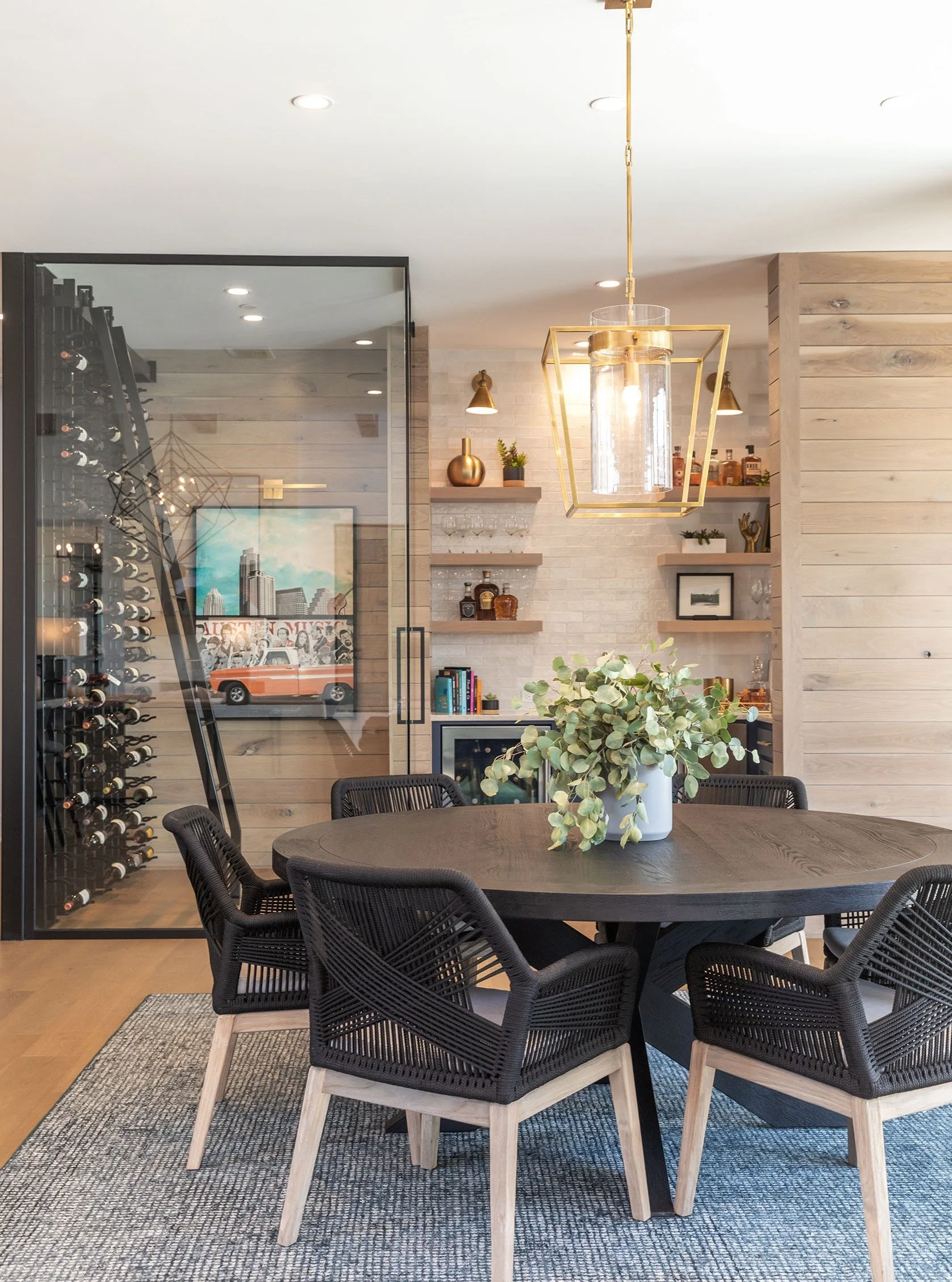Some spaces don&rsquo;t need bold color to make a statement.
This one leans into contrast, texture, and scale instead.

The black woven dining chairs, warm wood tones, oversized lantern, and glass wine wall create a space that feels elevated while st
