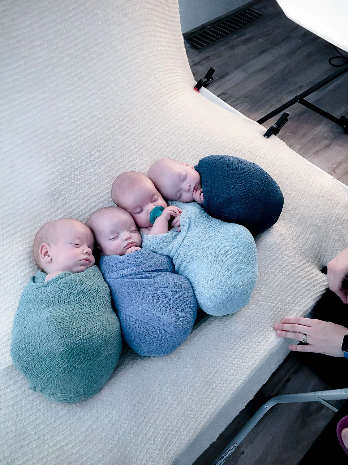 Four swaddled babies sleeping on a cream blanket behind the scenes