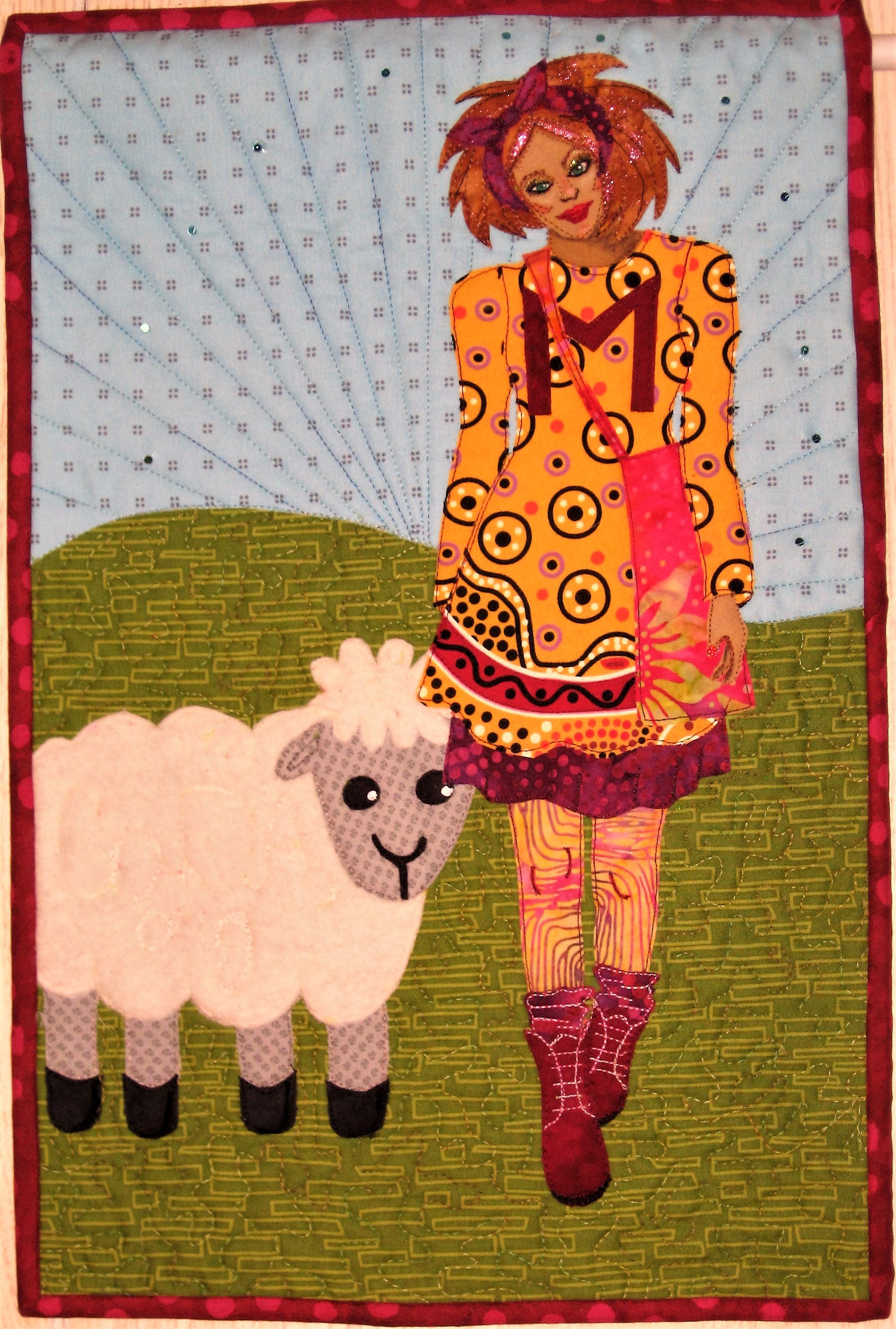 My Facebook art quilt group Art Quilts Around The World has it's reveal today. The theme is nursery rhymes with a back story or plot twist. I chose Mary Had a Little Lamb and the lamb was co-dependent and that's why she followed Mary to school!! Haha!! I decided to make Mary a high school student with a cute fit and flare dress and petticoat, leggings, slouch sox and Doc Martin boots! I selected the local Menominee high school colors of maroon and gold for the color scheme of Mary's outfit. Locally anyone supporting the local high school wears a maroon "M" on the front of their dress/tee shirt etc. The "M" could also represent Mary's first name initial. The lamb was created by me Googling lamb clip art since I didn't really know what a lamb looks like. For the fleece I used quilt batt-not "as white as snow" but I loved the fuzzy texture! I thread painted CoDA.org on the lamb's body to share about the national organization which helps people (lambs?!) with co-dependency. I had fun stitching the details of Mary's garment especially the boot details.