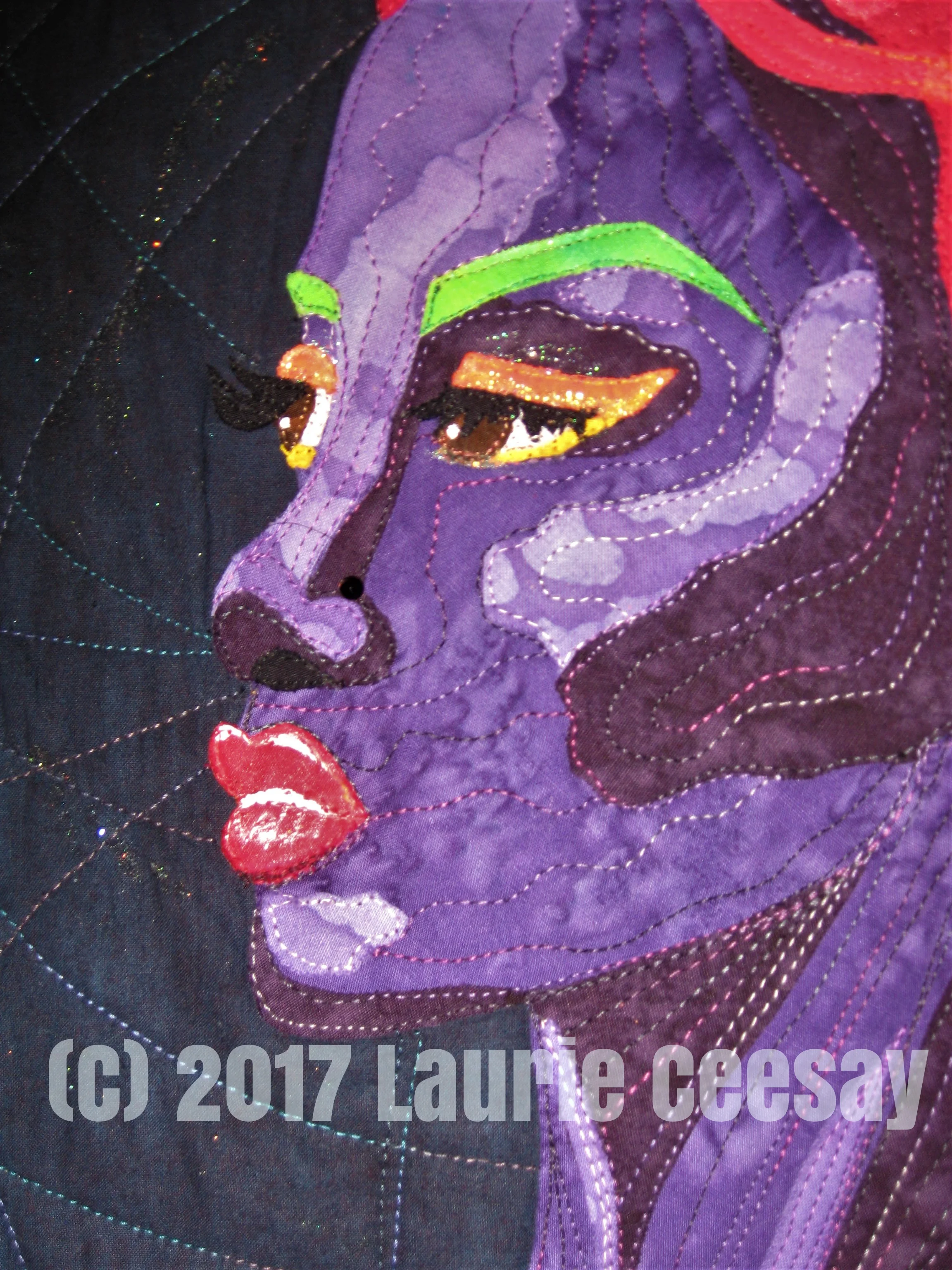 In the close up of the face I added neon loose glitter as eyeliner and a dab of purple glitter poster paint from The Dollar Tree on the eyelids. I used white fabric paint to define the mouth. it is not noticeable in this photo but I used three dark purple beans/sequins for a low contrast color earring and a dark purple rhinestone for a nose piercing. I used some blue glitter nail polish on a small scale to highlight the dark blue background. I quilted large swirly circles which happened thanks to my kitchen! I pulled a large round pizza pan, a large Tupperware lid and a dinner plate to mark the circles! One has to be creative!!
