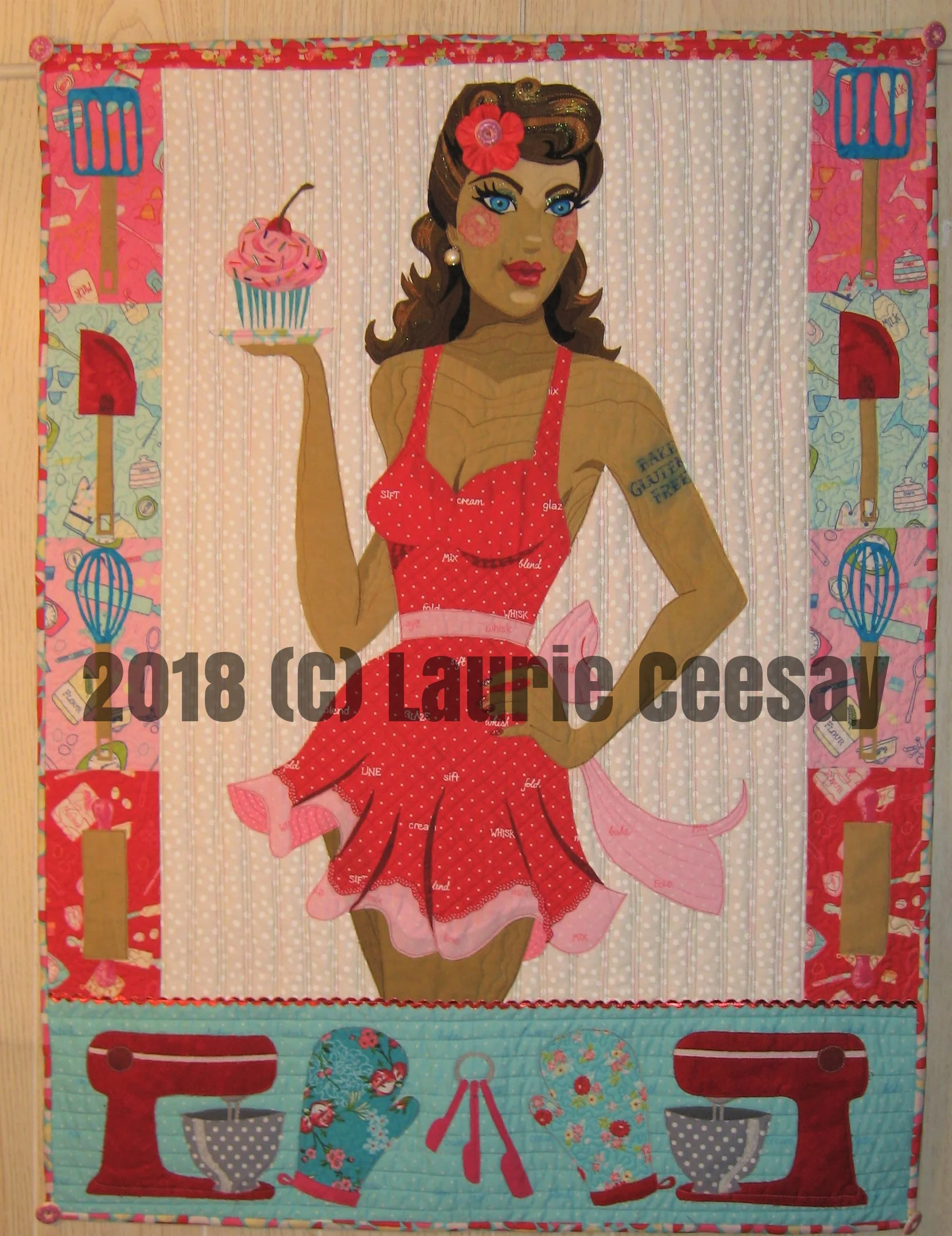 The Wisconsin Quilt Expo is held in early September in Madison and they have been having a special challenge at their quilt expo and the theme for 2018 is called Bake Off. I immediately thought of a pin up girl in the kitchen when I designed this quilt. The only rule was the size of 30" wide by 40" long which is typically larger than I work. The pin up girl is wearing a sexy ruffly apron and holding a cupcake. I added baking utensils to the sides of the project to get the 30" width. I added a wide bottom area with mirror images of a Mix Master, oven mitts and measuring spoons. This project began with a purchase from www.craftsy.com where I purchased a variety of fabrics with a baking theme. I used a print with baking words in the apron, sash and bow. I added a red and white trim near the bottom edge.. The fingernails received red glitter nail polish. 
