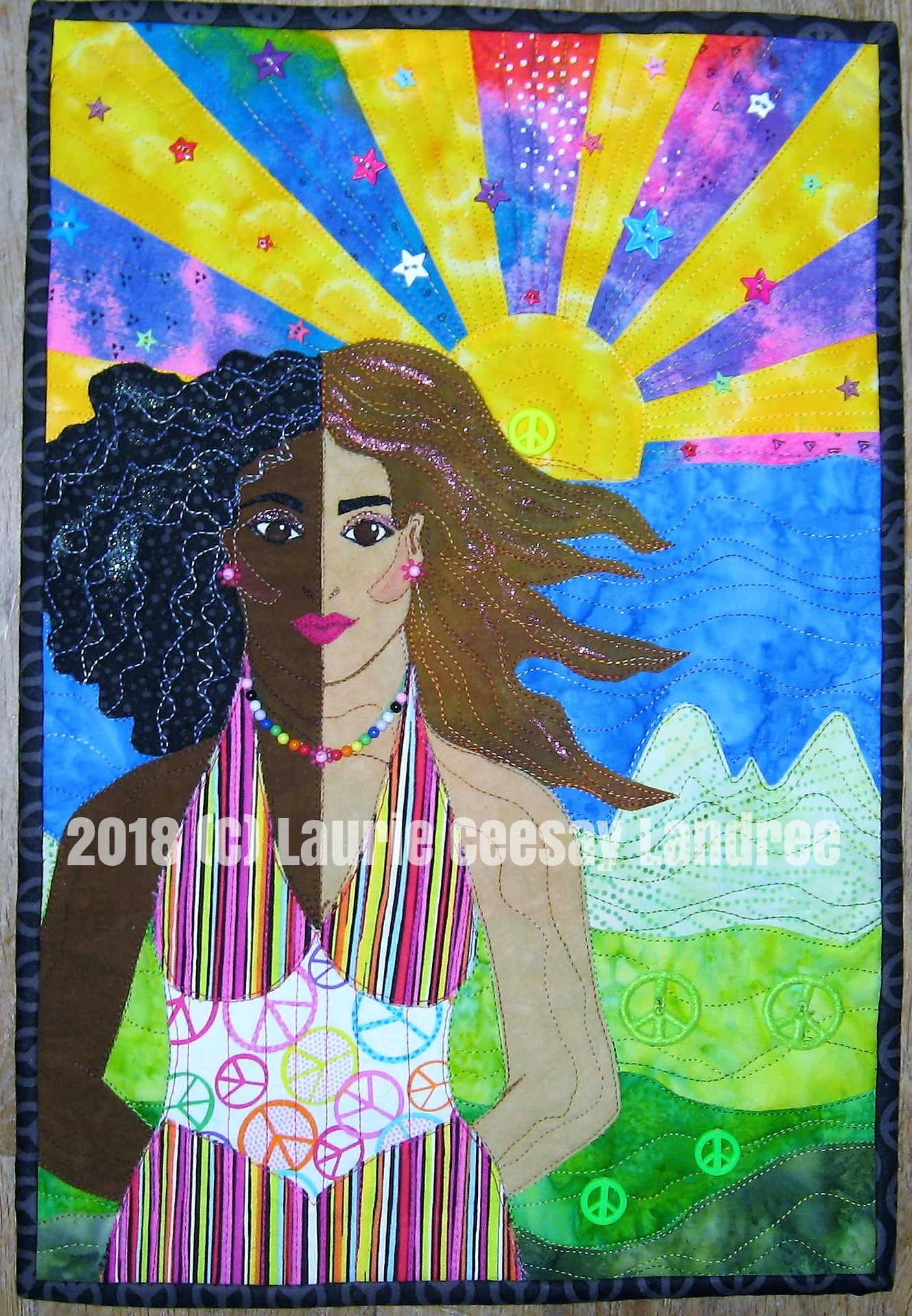My Facebook art quilt group called Art Quilts Around the World had a new challenge due Sept. 30, 2018. I had a very busy August and September including a small wedding for my boyfriend of 13 years. We got married on October and I am Laurie Ceesay Landree in the quilting world. I knew I was not going to complete the challenge on time so I postponed it ad continued after the wedding and before I went to Houston. The challenge was called Imagine based on however we interpret the John Lennon song of the same name. I interpreted the title by imagining racial harmony. I love the 1960s-1970s artist Peter Maxx and used my version of his landscapes with the strong sun and rays of the sun with lots of colorful stars in the sky with water, grass and mountains. Then I chose to divide a female motif in two with one side as a black woman and the other side as a white woman. I used the peace sign as an image of unity and harmony. I finished the quilt in mid October then chose to not embellish it and I used it in my Mixed Media Forum demo at the International Quilt Festival last month in Houston as an example of a project ready to embellish. I explained my thought process and had potential embellishments to demo. I returned home a week ago from Houston and I was able to hand sew lots of star buttons, beads for jewelry, nail polish in the hair and on the face for bling. I had a few green felt peace sign buttons and a few green and one yellow peace sign buttons for the landscape and the sun. Very colorful and whimsical!!