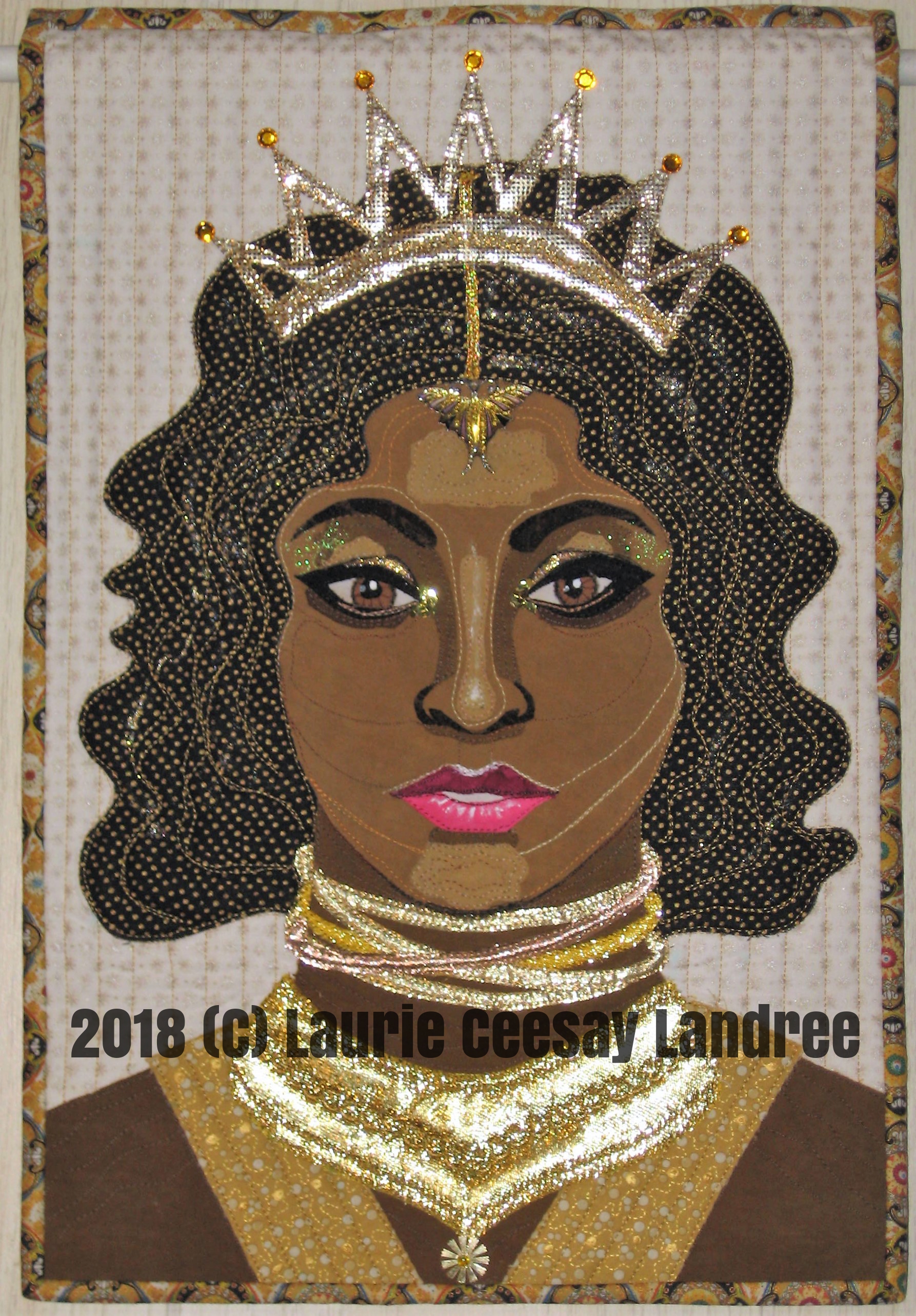 My Facebook art quilt group’s current challenge is due for revealing today. The theme was Numbers but with a twist of using a song, book or saying title. I somehow had the Bruno Mars song 24K Magic pop into my head and I thought about a portrait quilt with the use of a bunch of metallic golds and a woman who represents an African/Nubian queen. I pulled from my stash all potential lames and gold embossed fabrics. I wanted a crown on the woman’s head and a lot of necklaces and a collar type thing around her neck. I frequented Pinterest for ideas and ran with what I liked. I embellished this quilt with a sequin/bead, chunky gold glitter, gold nail polish, gold Dollar Store poster paint, fabric markers, white matte fabric paint, rhinestones, grosgrain ribbon and a repurposed earring hanging on the forehead. I had more than enough trim and bling to make this work so I had to edit out some of the goodies.