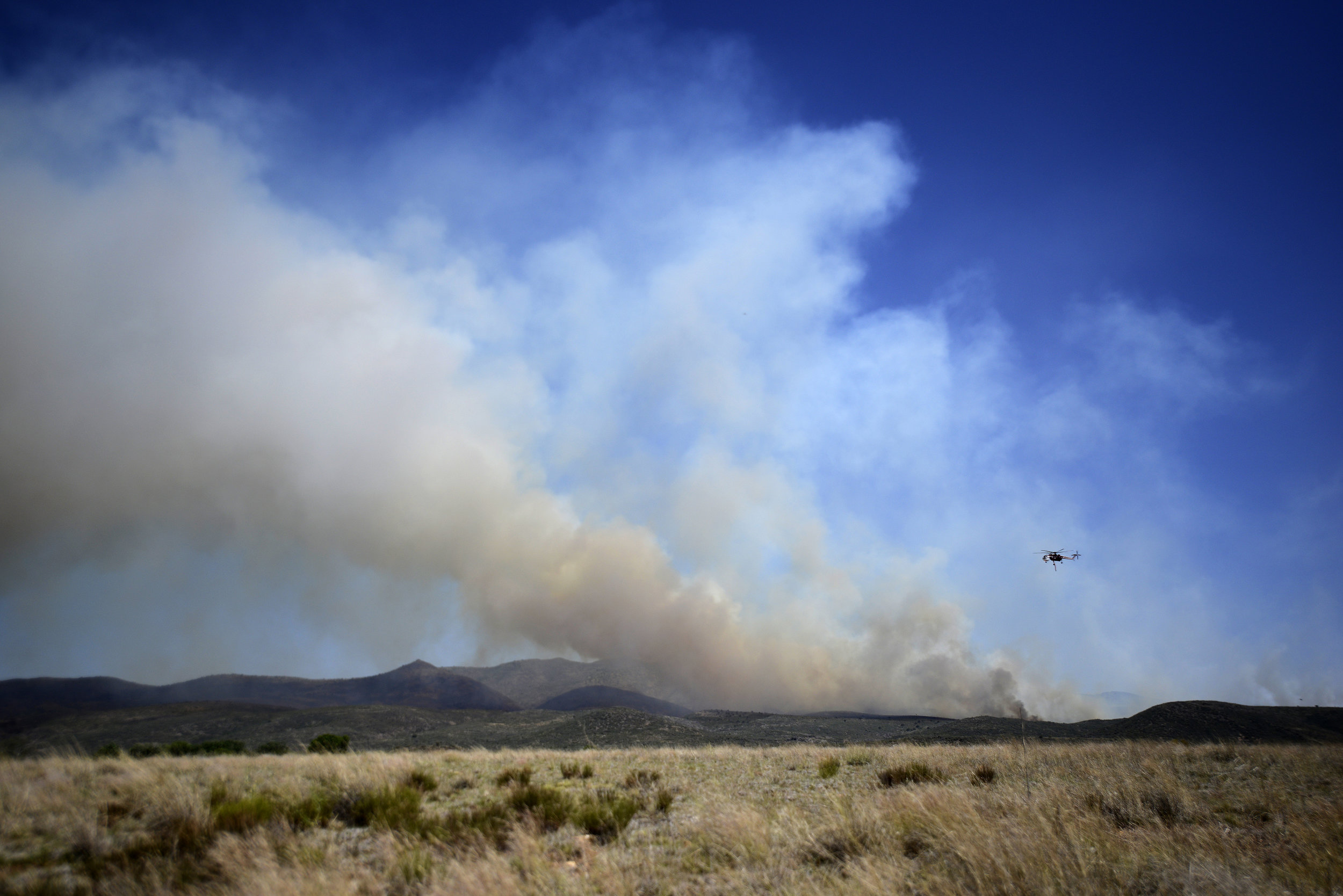  A helicopter flies over plumes of smoke to pour water on a wildfire about 60 miles northwest of Phoenix on Thursday. The fire began Wednesday near Yarnell, Ariz., a town that just three years before lost 19 elite firefighters in another blaze. 