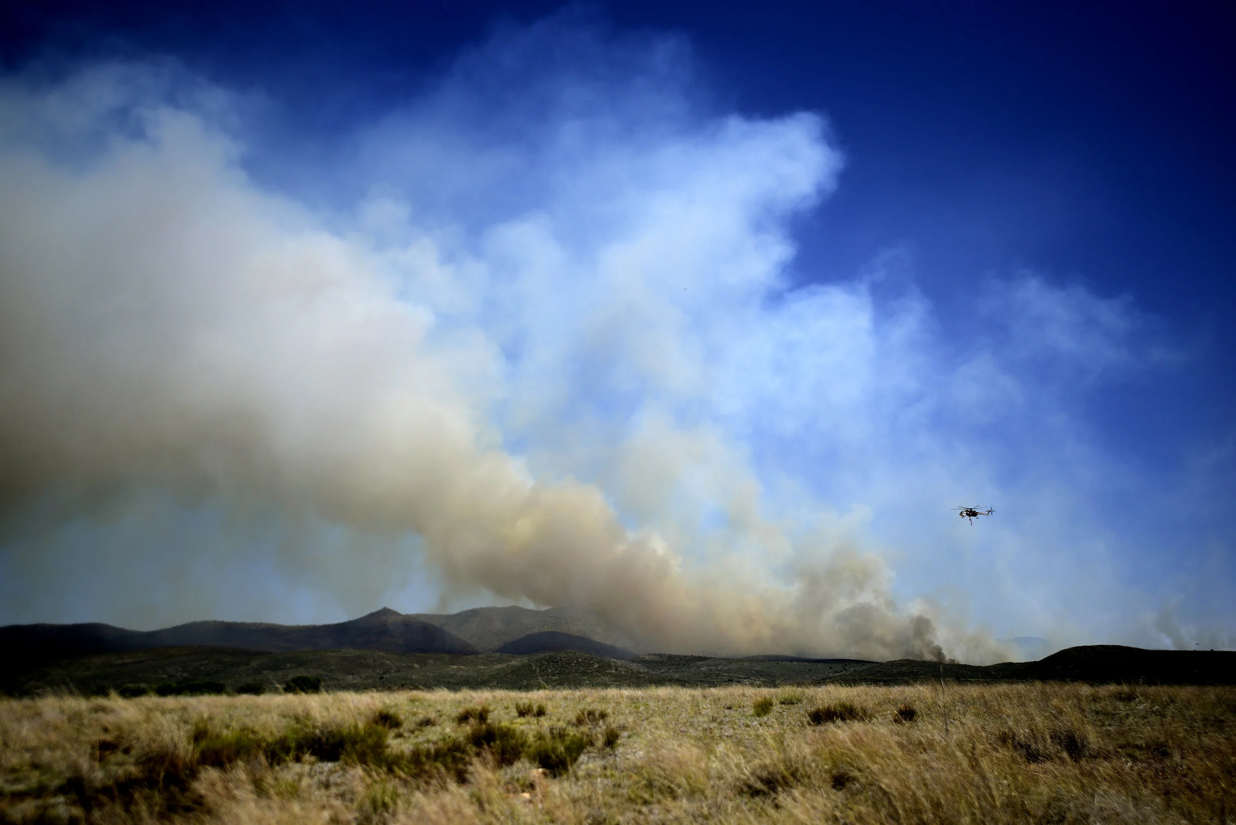  A helicopter flies over plumes of smoke to pour water on a wildfire about 60 miles northwest of Phoenix on Thursday. The fire began Wednesday near Yarnell, Ariz., a town that just three years before lost 19 elite firefighters in another blaze. 