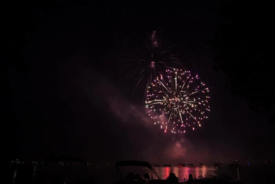 Fireworks display over a body of water at night with boats in the foreground. Photographed by Kayla Duffney Creative.
