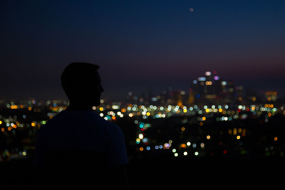 Silhouette of a person overlooking a blurred city skyline at night with colorful city lights. Photographed by Kayla Duffney Creative.