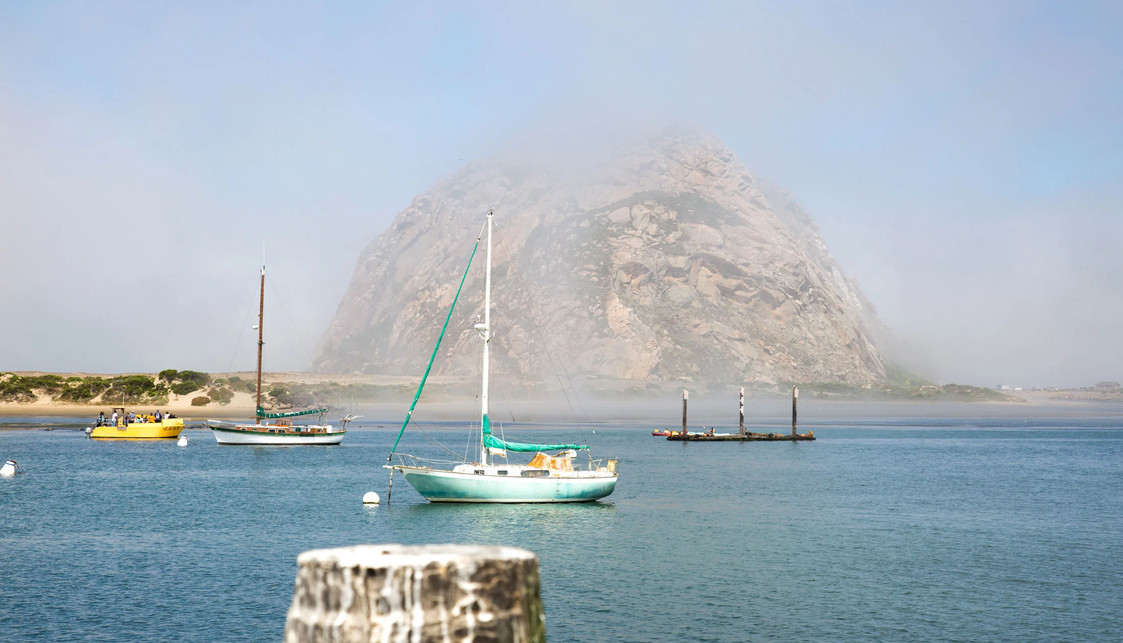 Boats docked in a harbor with a large rocky mountain in the background shrouded in mist or fog. Photographed by Kayla Duffney Creative.