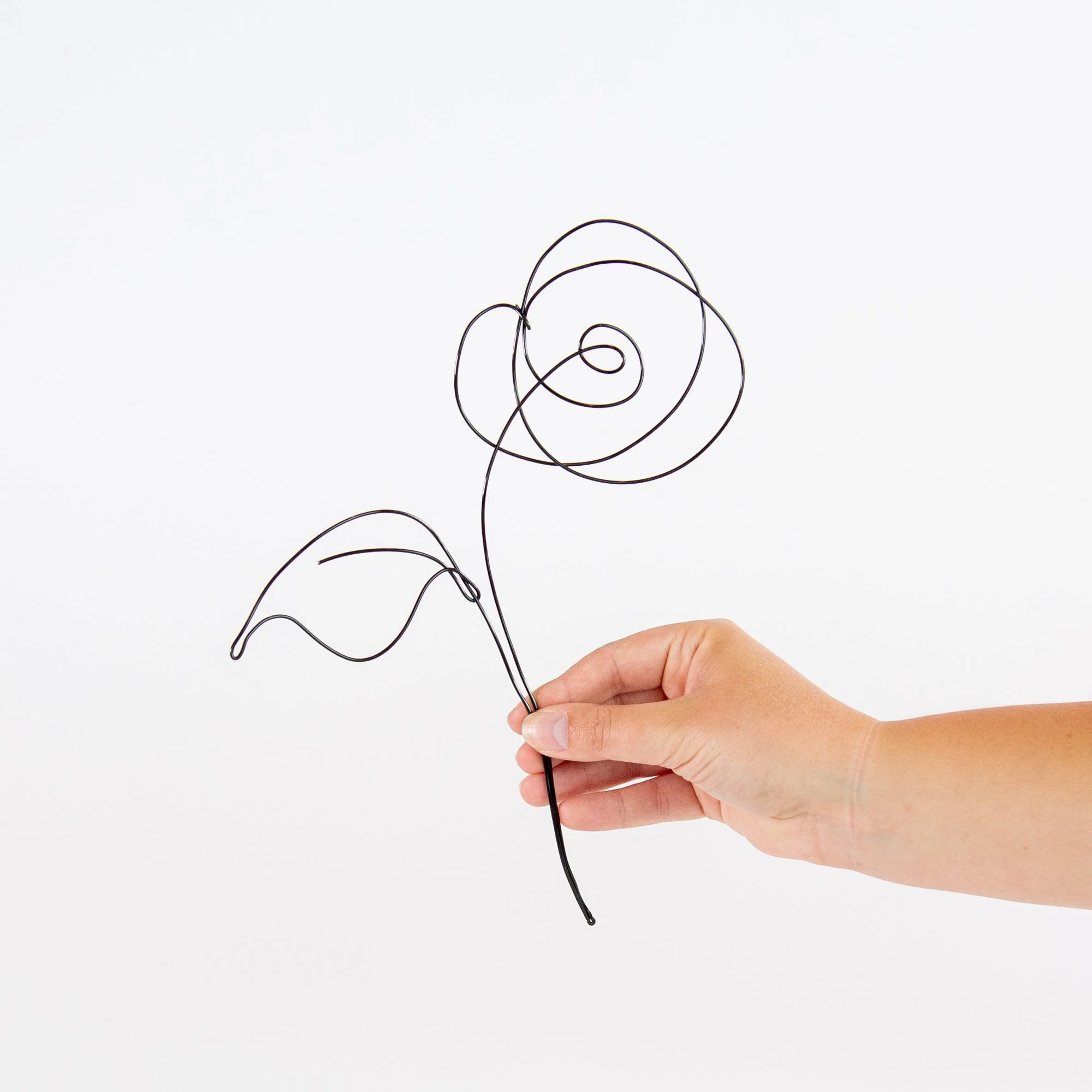A hand holding a wire sculpture of a rose against a white background. Product photography photographed by Kayla Duffney Creative.