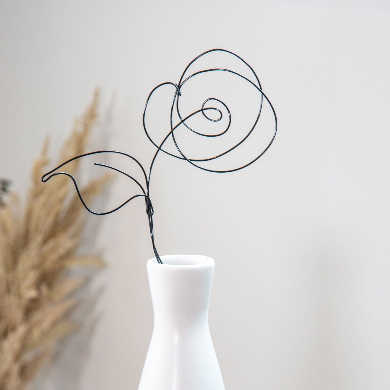 A white vase with a black wire sculpture of a flower. Product photography photographed by Kayla Duffney Creative.