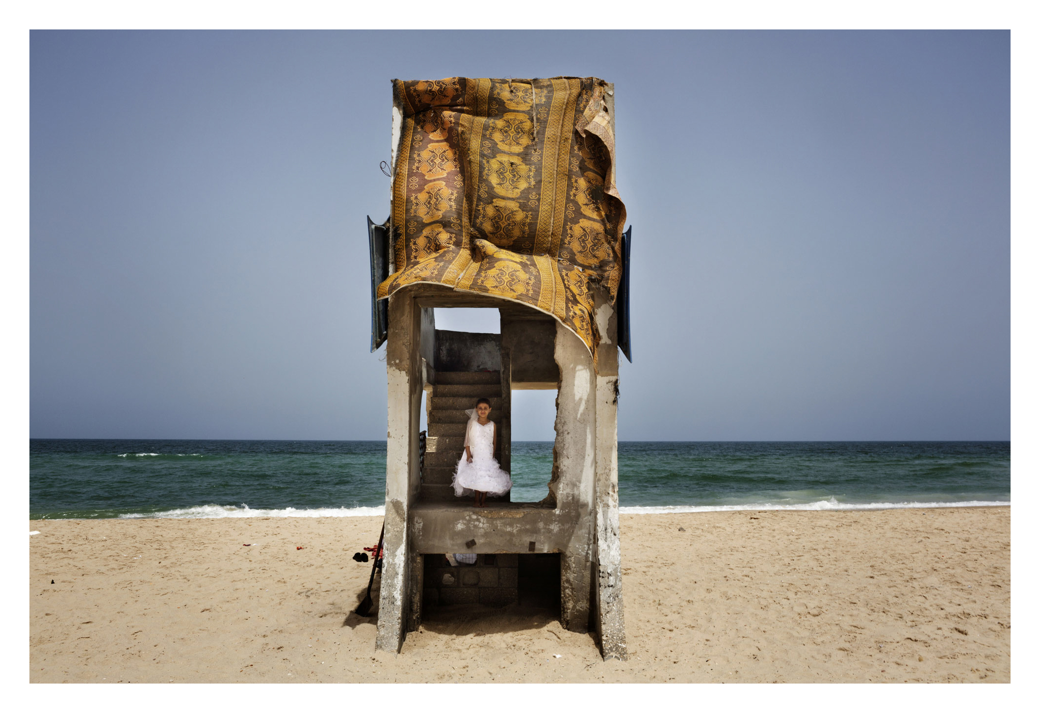  A young girl plays on the beach in the party dress she wore the night before at a wedding, at the Deir al-balah Refugee camp in Gaza. 