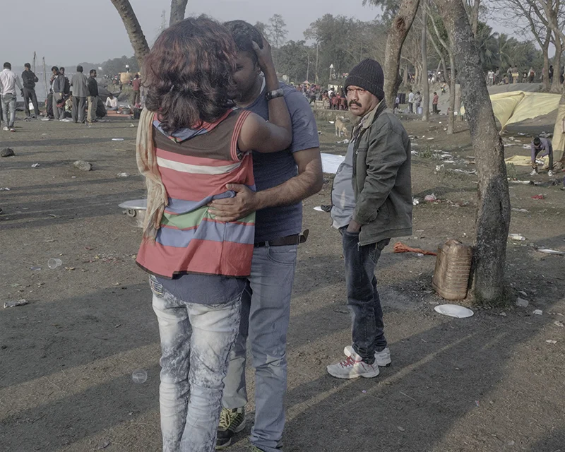 India, Falta, January 2017. A transgender individual obliges a drunk picnicker under the disapproving glances of another man. A group of transgender persons went about the crowds usually to dance with them in exchange for cash.