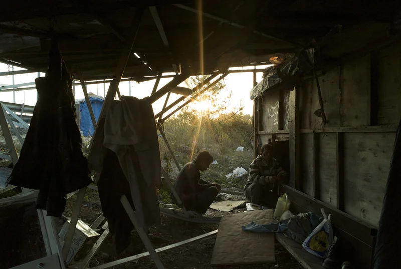 Greece, Patras, November 2011, Under a structure of scaffolding and salvaged partition walls, a teenage Afghan boy crouches down outside a shelter pitched under a bend in the highway on the main Athens to Patras road.