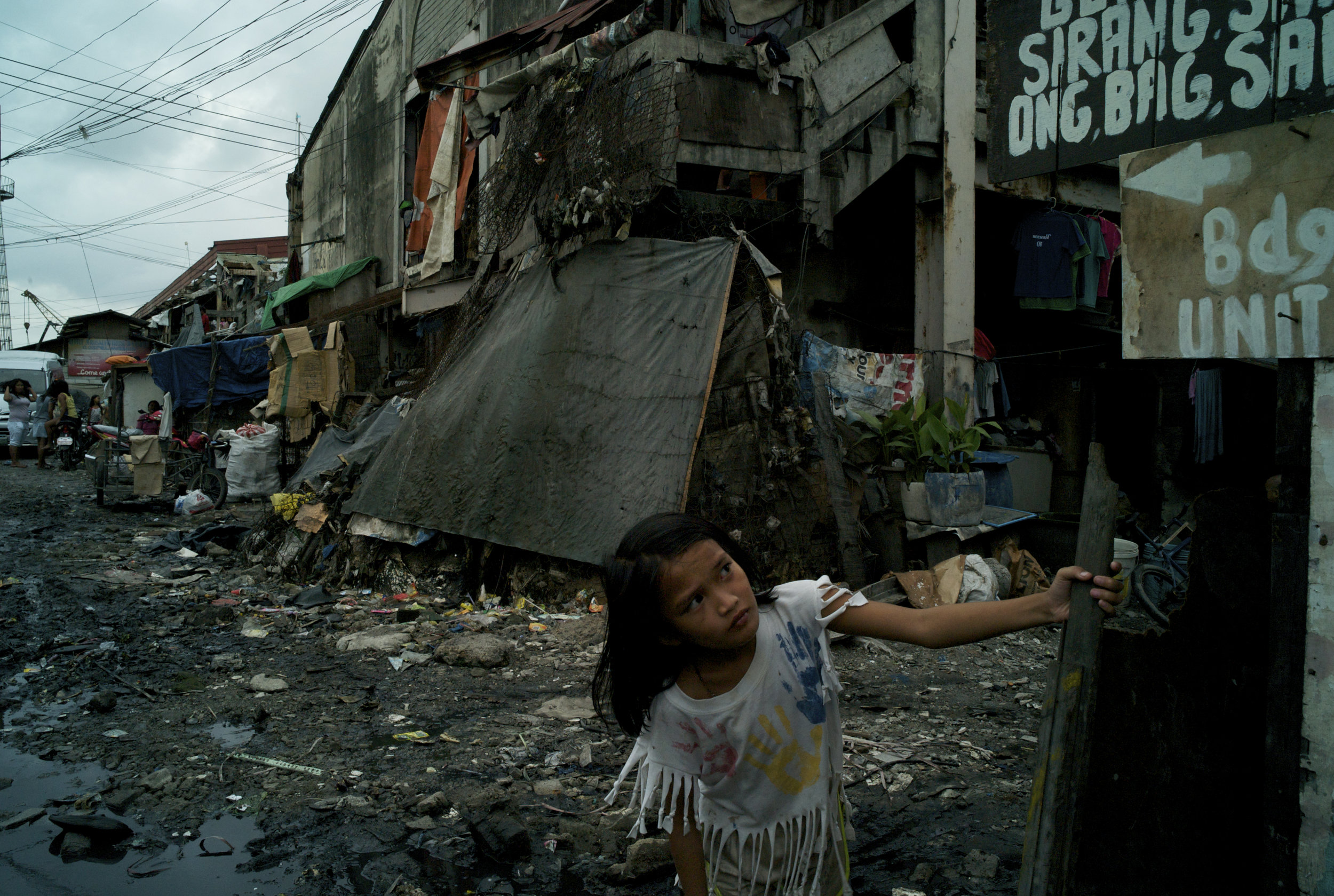  MANILA, THE PHILIPPINES; JUNE 2103 
-	Swinging from a wooden post, a young girl makes her way through the flooded, rubbish strewn streets that crisscross the temporary government tenements of Aroma. Originally designated as a short-term resettlement