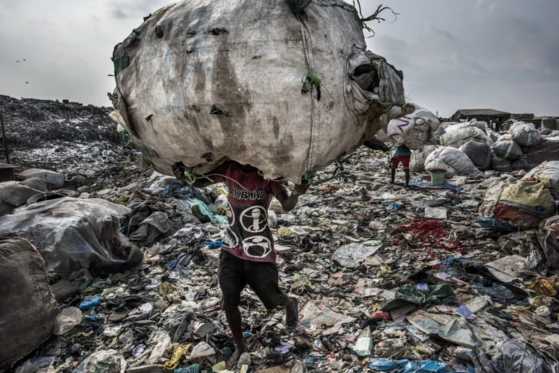 Nigeria, Lagos, 27 January 2017
A man carries a huge back of pet bottles collected for recycling at the Olusosun landfill.
The Olusosun landfill in Lagos receives between 3-5000 tons per day and is about 45 ha in size. About 5000 scavengers work here and often also live. They collect anything that is recyable like plastics, textiles, electronics, paper etc. The problem is that the landfill is full and the city wants to close it down. The question is where it will go, there are no incinerators and the infrastructure to formally recycle is lacking. There is one other landfill, but it needs to close as well.
Remarkable is that the landfills in Lagos smell less compared to other landfills in the world: Nigerians throw away less food, because they either finish their plate or feed it to the animals.
Kadir van Lohuizen / NOOR