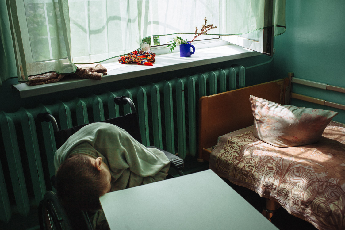 Residents of the psycho-neurological residential care facility for the elderly and disabled #3 in his room. May 24, 2016, Minsk, Belarus.

Many of the residents lie all the time, which causes atrophy of all muscles. In the orphanage there is no reha