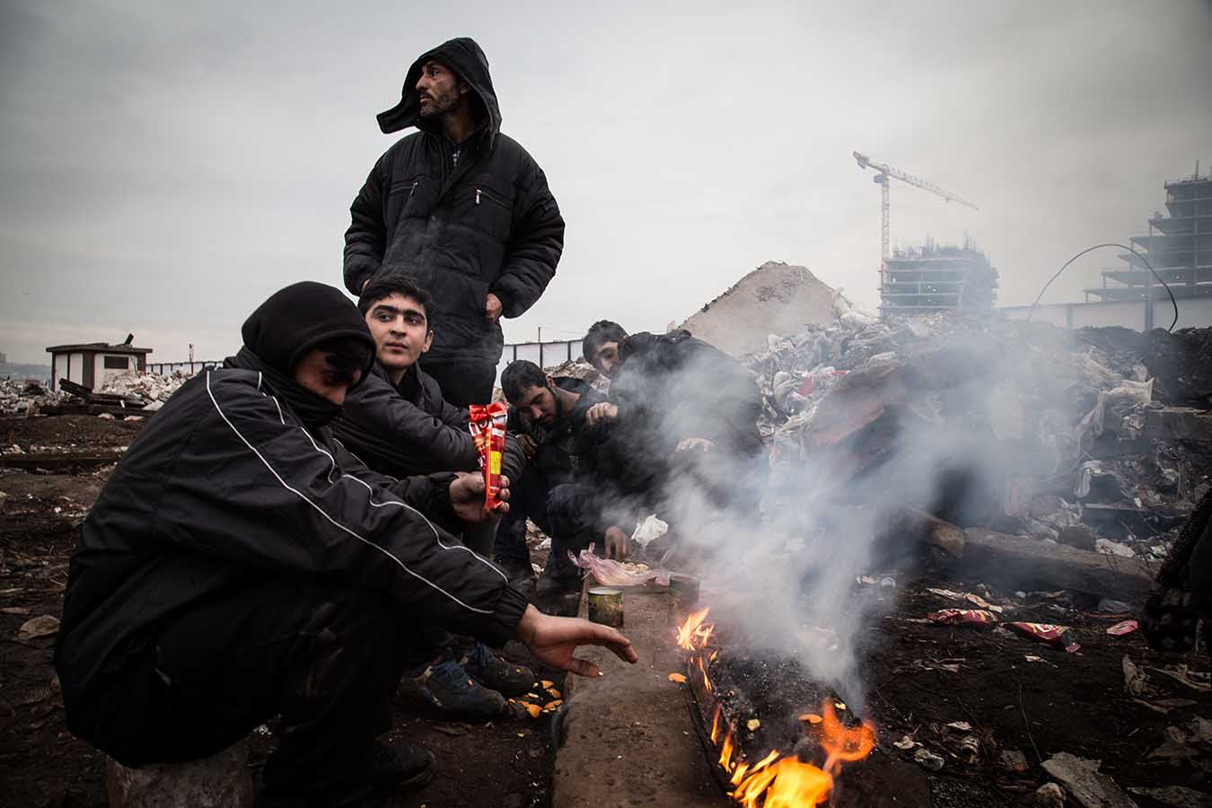  Afghani migrants warm themselves sitting around an open fire, just outside the “Barracks”, a derelict complex of industrial building in the area of Belgrade’s Central Station.  Since Summer 2016, an increasing number of migrants have been stuck in S