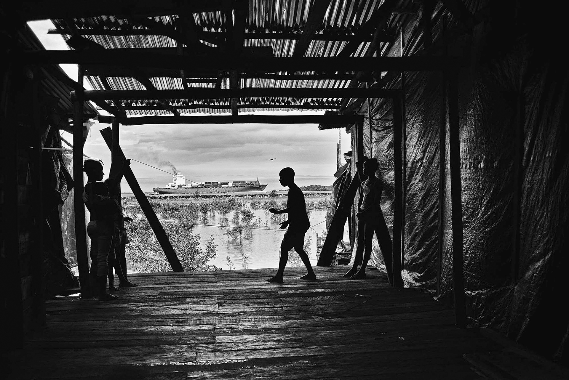  kids play in a shack in the SAn José barrio in front of a cargo coming in the port of Buenaventura. 