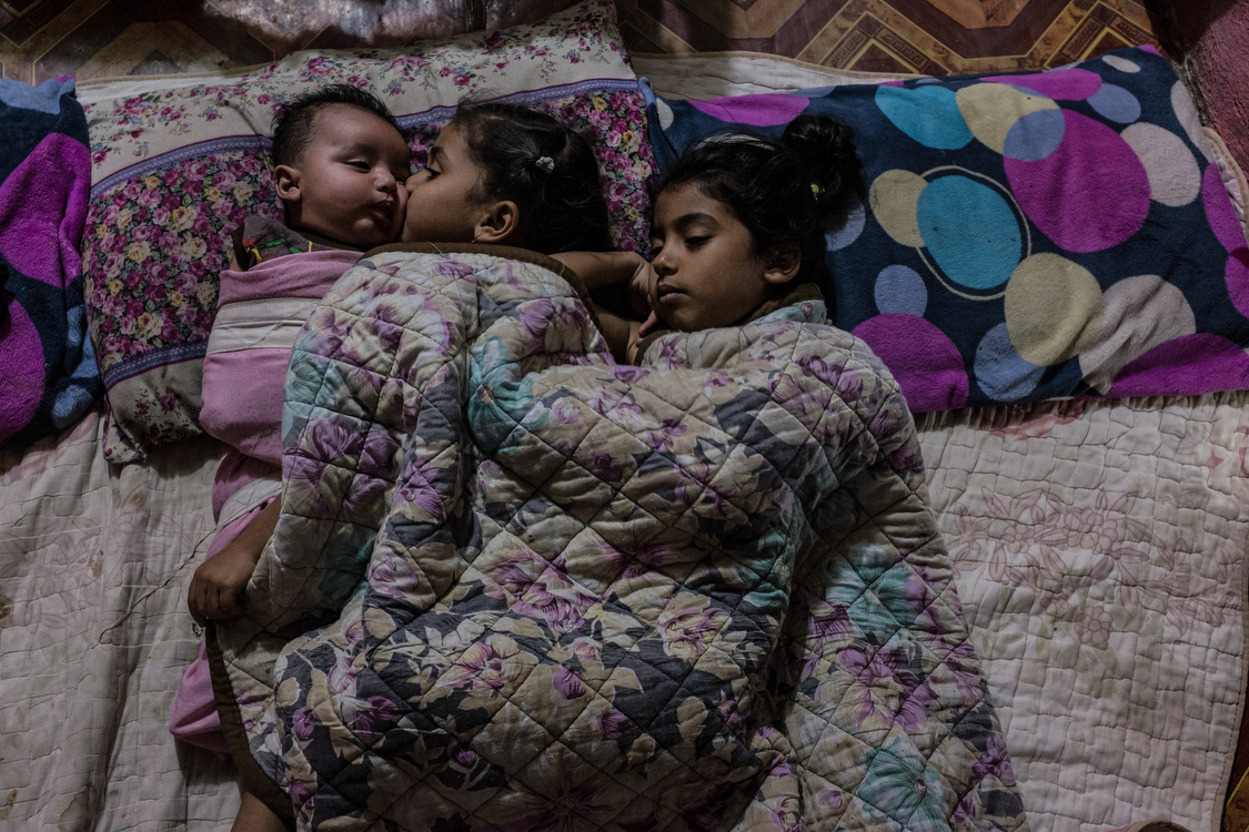  Fatma, Tiktum and Abdallah lay in bed just before going to sleep. The whole family sleeps on a blanket on the floor, in the main room of the house. 
Iraq, 15/10/2018 