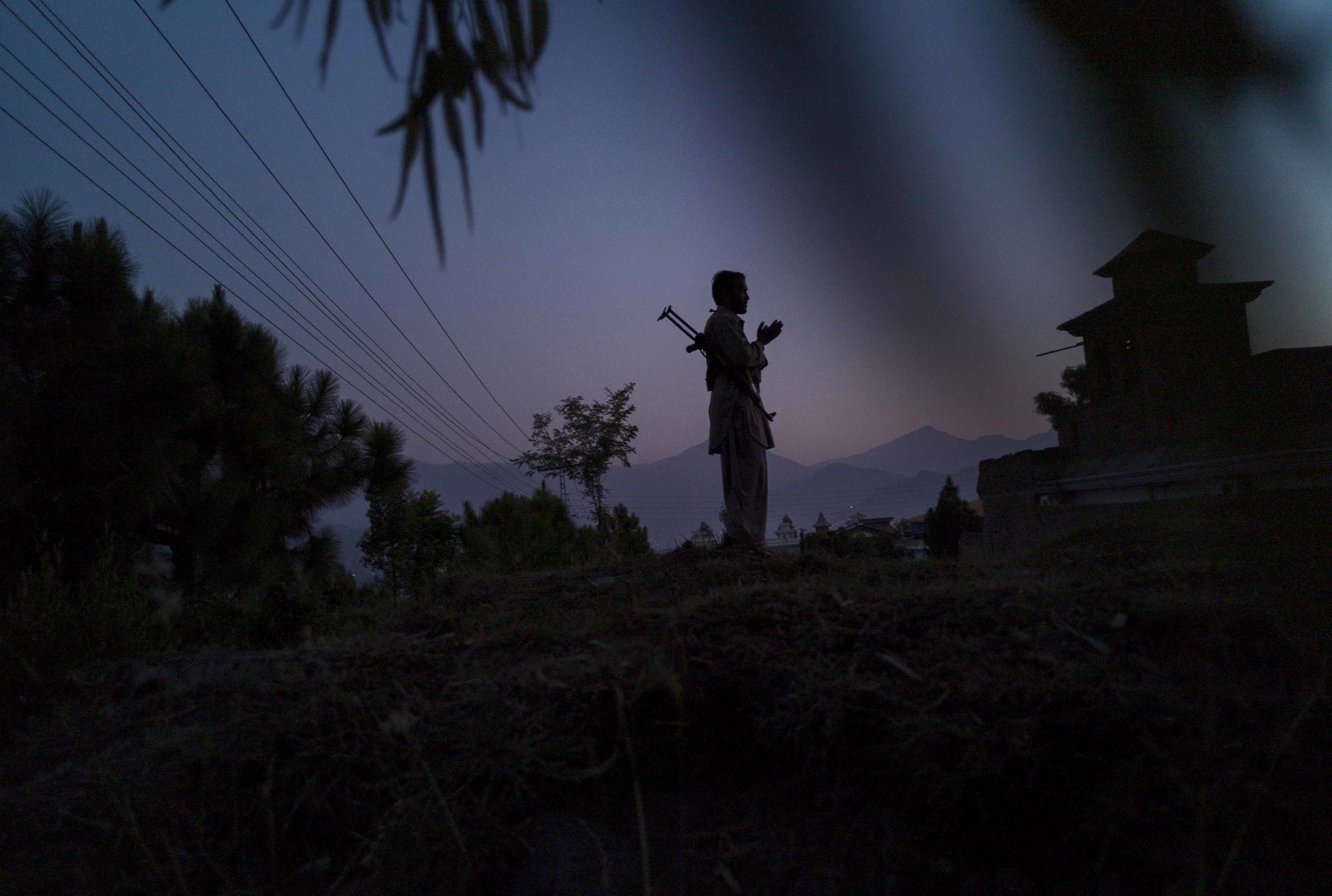  KANJU, PAKISTAN- SEPTEMBER 2009 
With his Kalashnikov rifle strapped to his back, a guard from a privte militia performs Isha Nimaz in a garden overlooking the Swat Valley in Kanju Township at dusk. Over the last week, the local population roused by