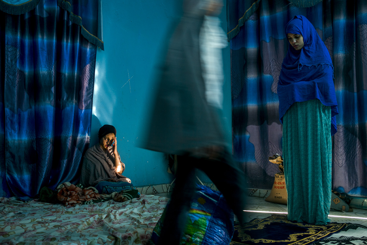  HARGEISA, SOMALILAND REGION OF SOMALIA - FEBRUARY 2018 
Partially shielding her face from a beam of light, Asmhan looks as her little sister Ayman makes her Asr prayers on the family’s single mat. Divorcing her husband in order to flee Yemen when wa