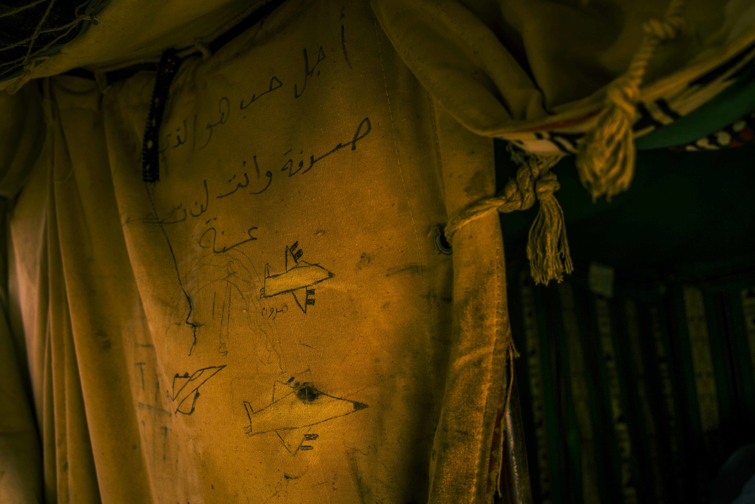  OBOCK, DJIBOUTI - MAY 2018 
Under Arabic graffiti that reads “You cannot search for the beauty of love, it comes to you” armed fighter jets have been drawn on the opening of a canvas tent in Obock Camp. Sketched by Yemeni refugee Mohamed Al Abid, th