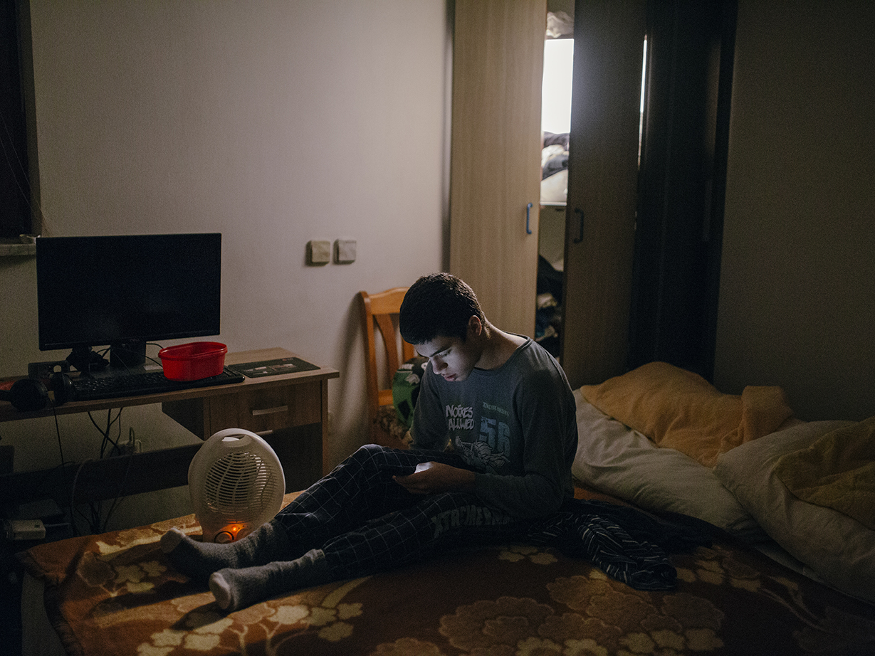  The conditions in the apartment where Nikola and Nenad live are not very good, it is very cold in the room where they sleep and spend their time. Nikola tries to warm up before going to school.  Kranj, Slovenia/2019
Photo/Vladimir Zivojinovic 