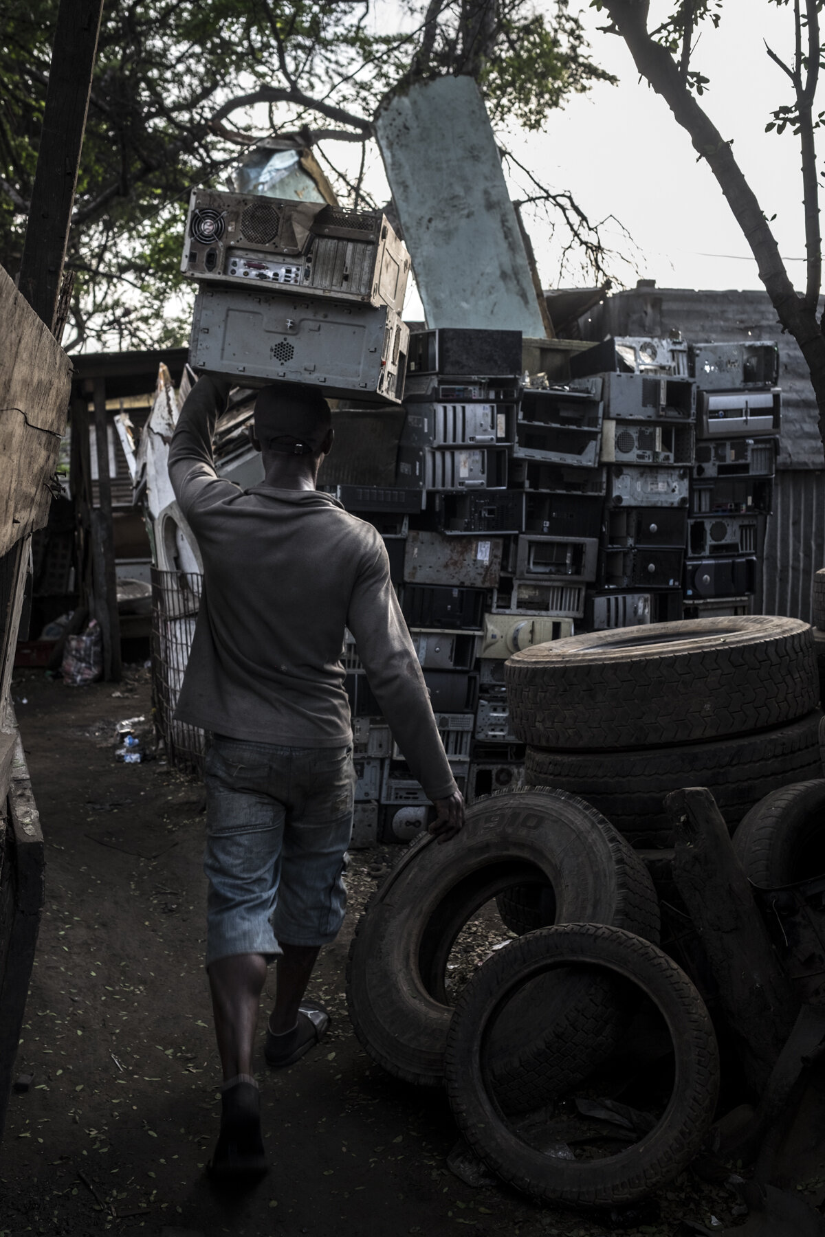  Ghana, Accra, November 2018. A worker in the Agbogbloshie scrap yard carrying parts of old computers. Workers with better finances go downtown to buy no working computers and appliances, in order to dismantle them, try to reuse the parts and, eventu