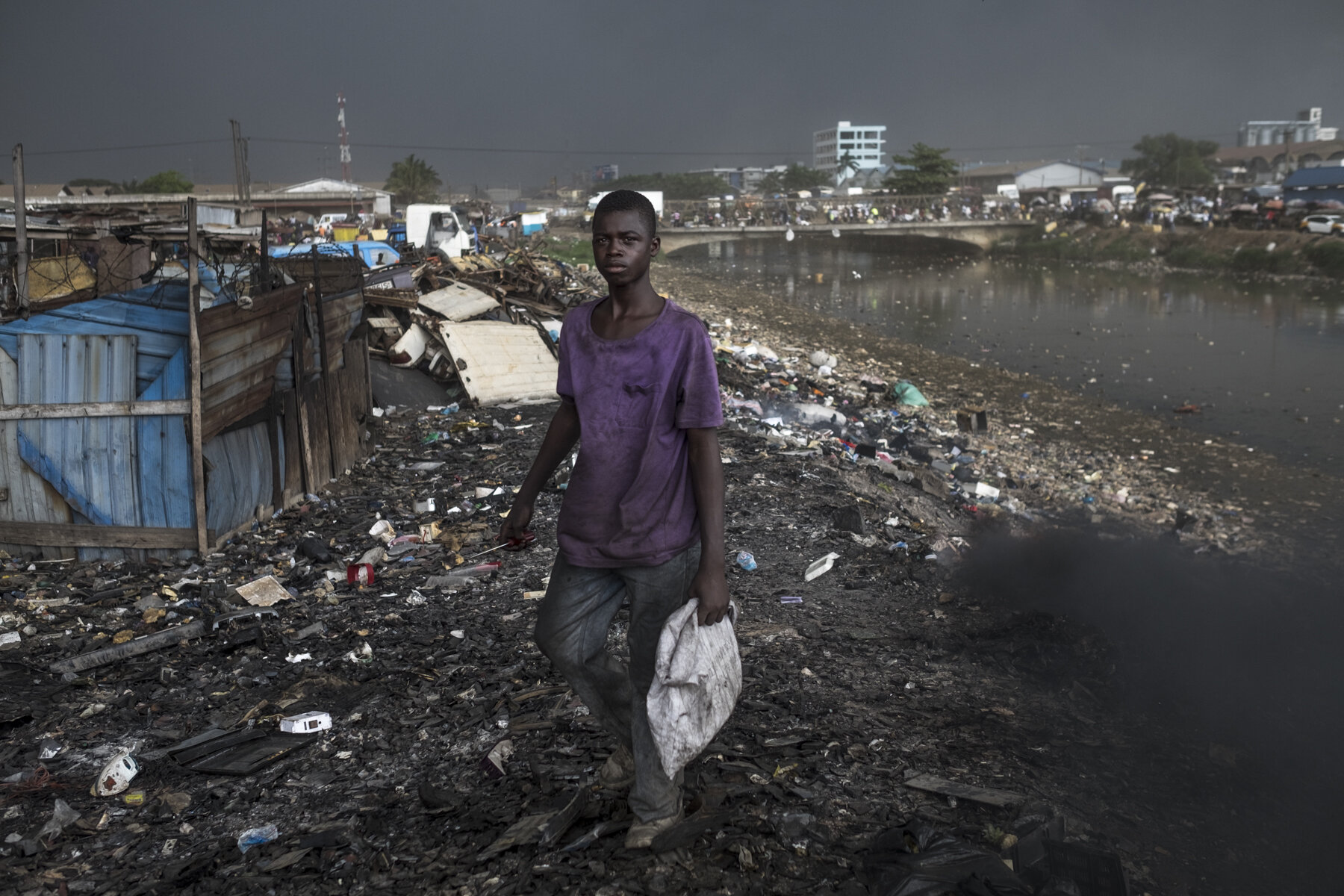  Ghana, Accra, October 2018. A worker picking up metal scraps by the Odaw River, in the Agbogbloshie scrap yard. 