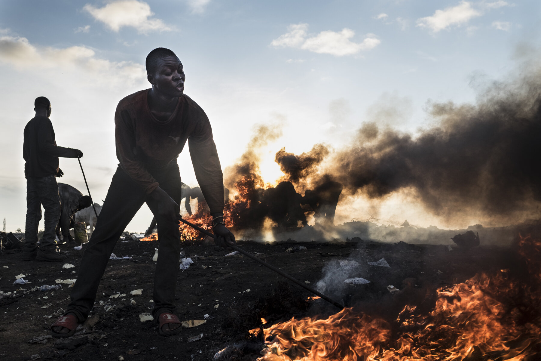  Ghana, Accra, October 2018. A worker burning appliances in the Kilimanjaro burning area of Agbogbloshie. The high temperature near the fire impede the use of protective mask. Workers, including children and young men, are constantly exposed to hazar