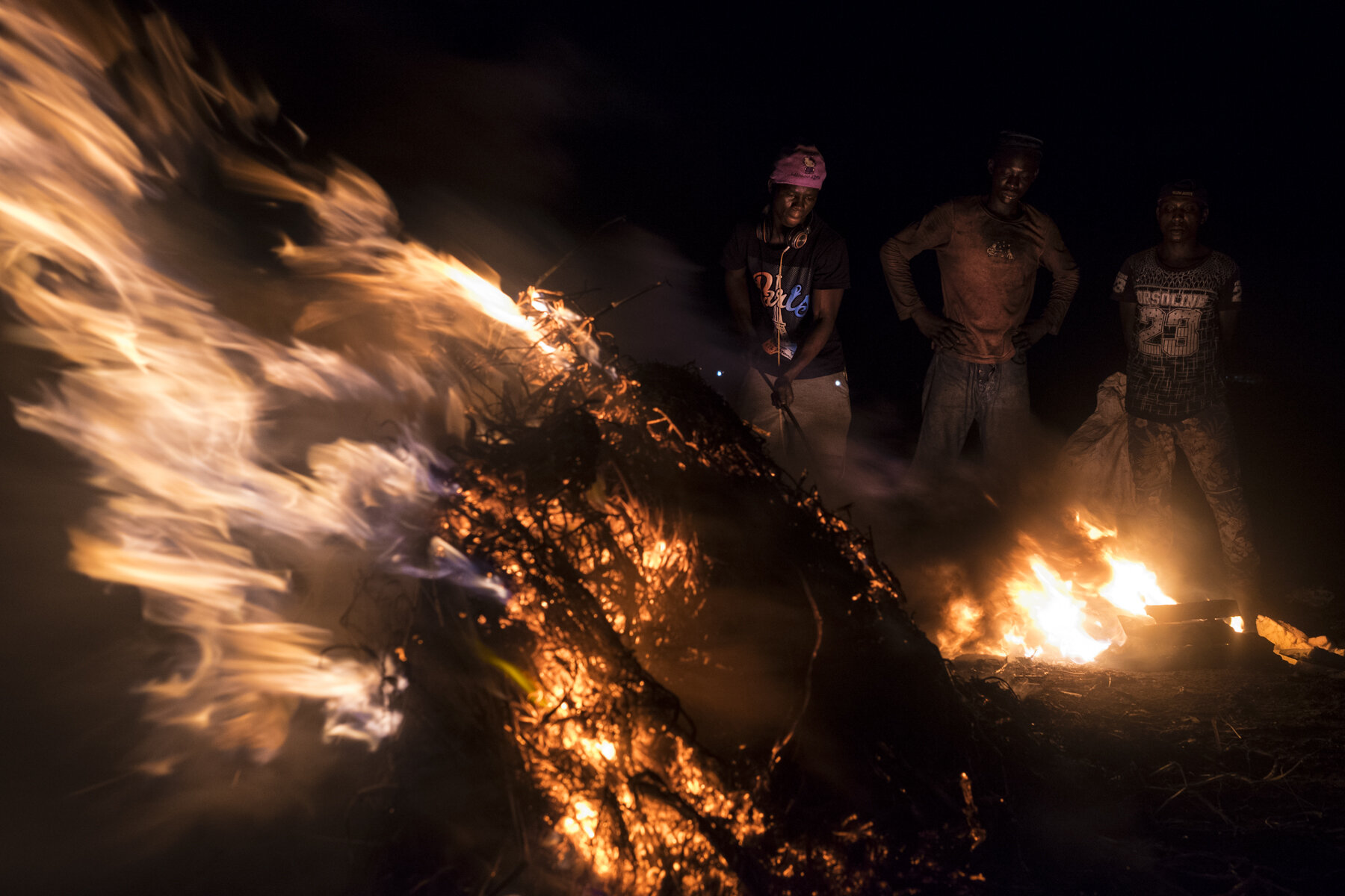  Ghana, Accra, October 2018. Alouta and Gaffarou are burning appliances and cables for another worker, in the Agbogbloshie scrap yard. Big fires are set at night to burn and extract as much raw material as possible, then go back in the morning and st