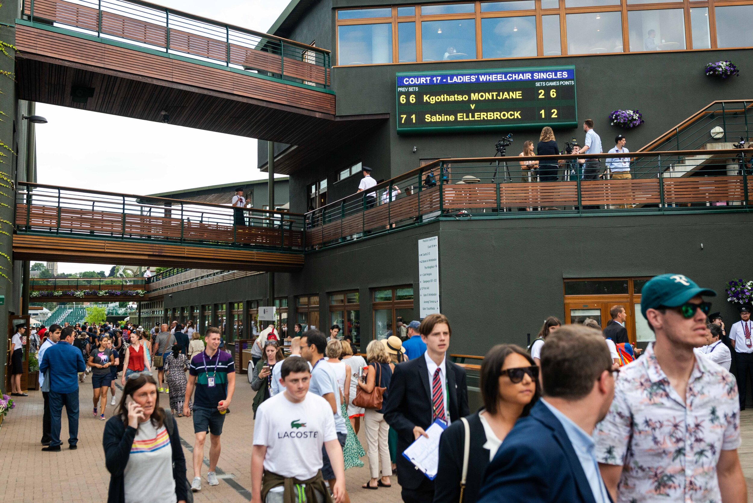  People walk through the area of Wimbledon. The result of the match between Sabine Ellerbrock and Kgothatso Montjane is shown on the display. 