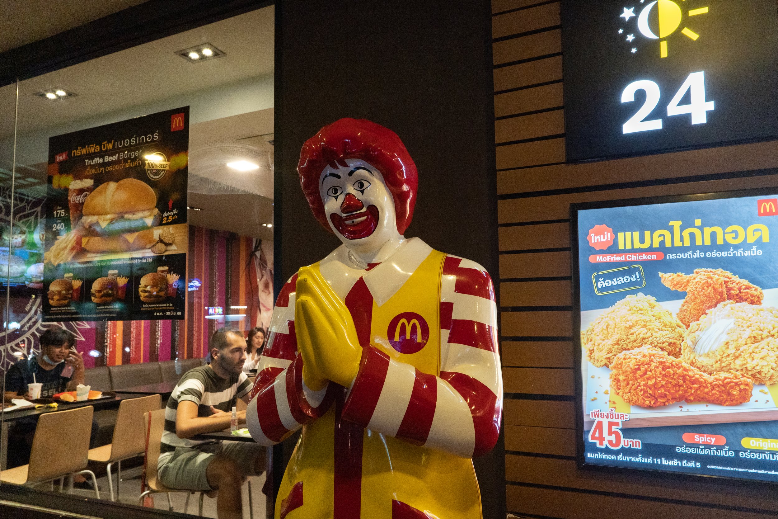  Thailand, Chiang Mai. 23 June 2023. a mascot of a western burger restaurant joins hands as a Thai greeting symbol meaning welcome, standing in front of a restaurant in the tourist area. The Western fast food business has spread across the globe and 