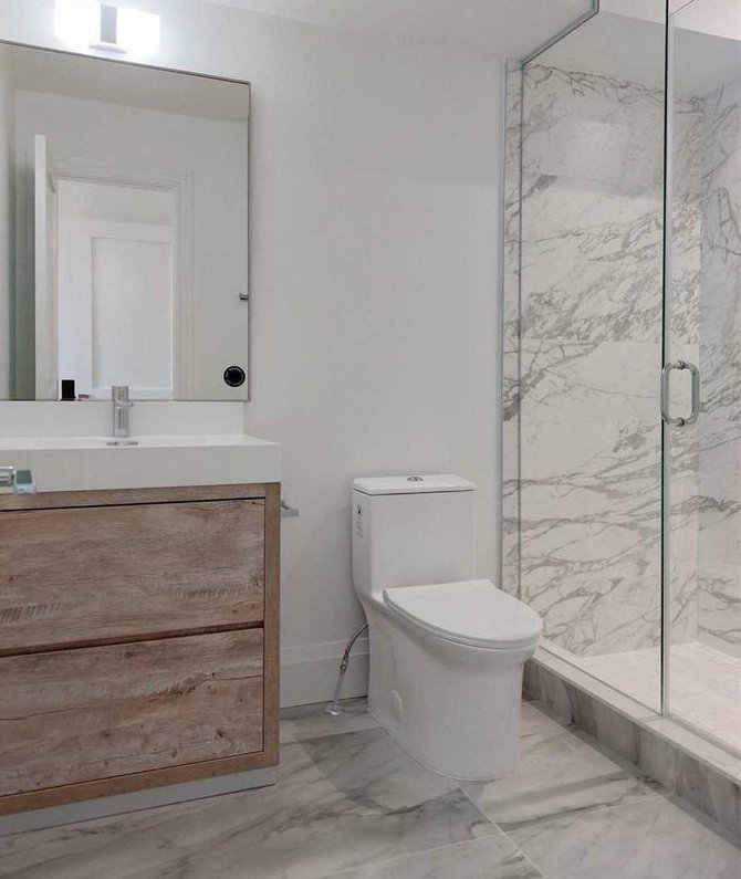 Modern bathroom with a wooden vanity, white toilet, and a glass-enclosed shower with marble tiles.