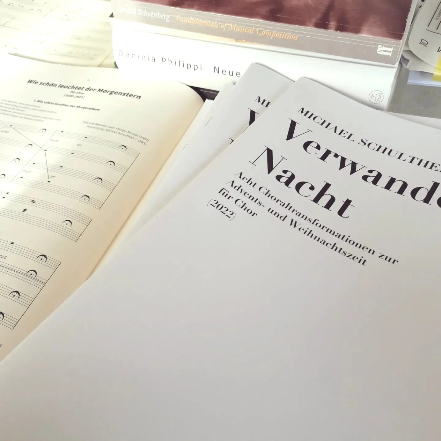 Ein Stapel Notenbücher mit dem Titel "Verwandelte Nacht" von Michael Schultheis, teilweise aufgeschlagen. Chornoten.
