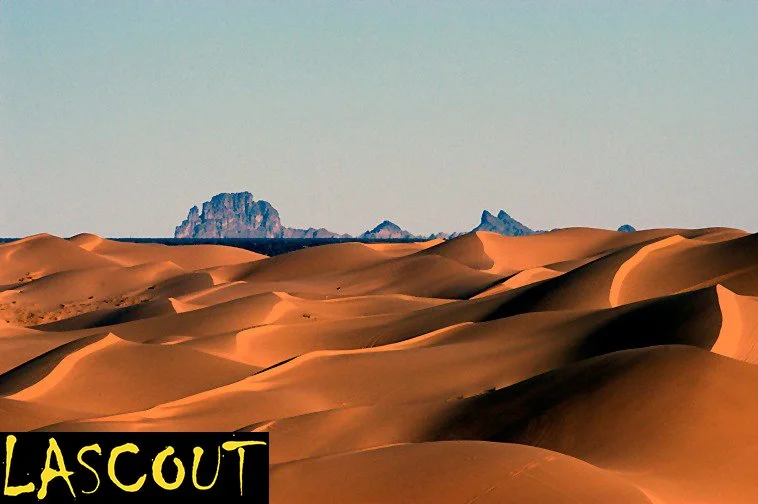 Desert landscape with sand dunes and rocky formations in the distance.