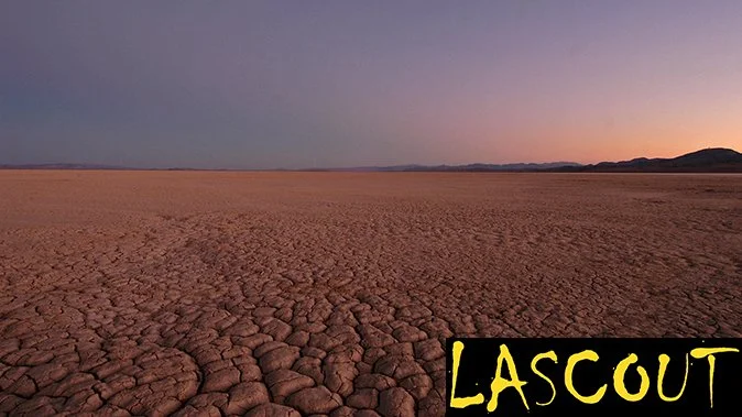 A dry, cracked desert landscape under a purple sky at sunset or sunrise, with mountains in the distance. The word 'Lascout' appears in yellow in the bottom right corner.