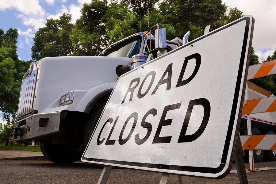 Large white truck parked behind a 'Road Closed' sign.