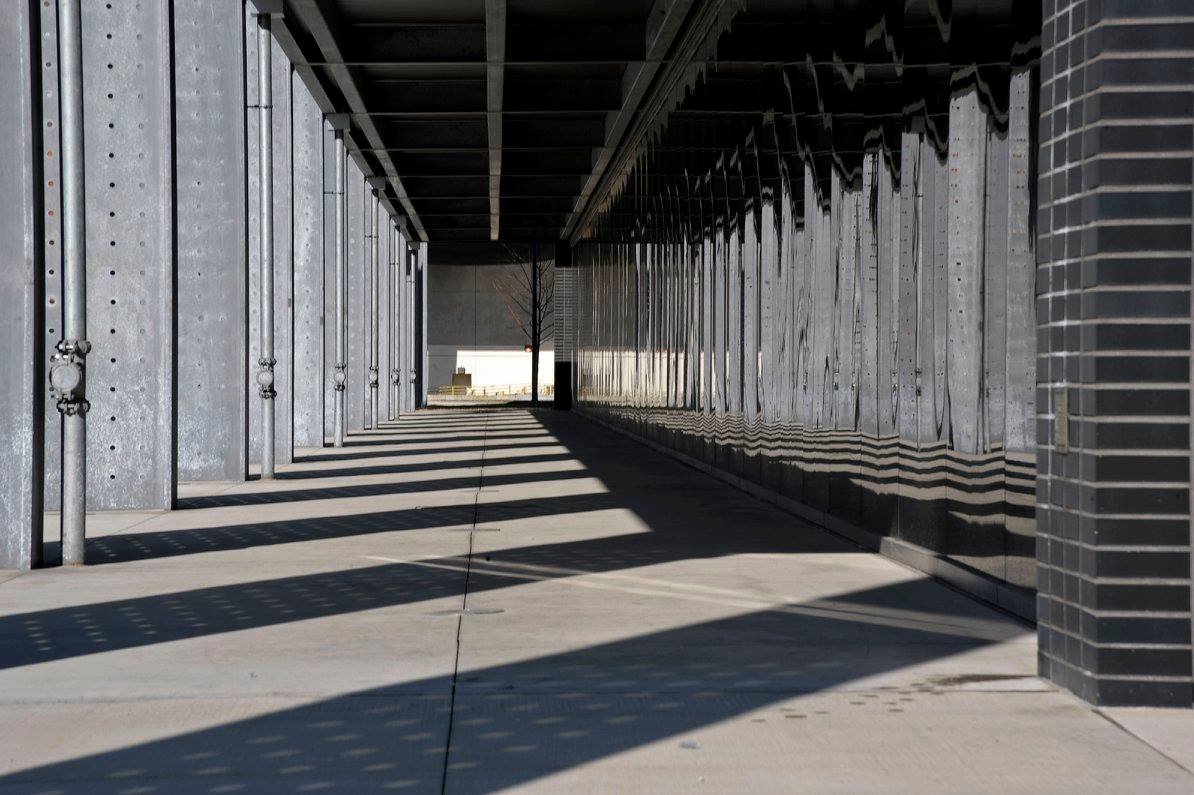 Empty sidewalk under a building's overhang, with shadows cast on the ground by the structure.