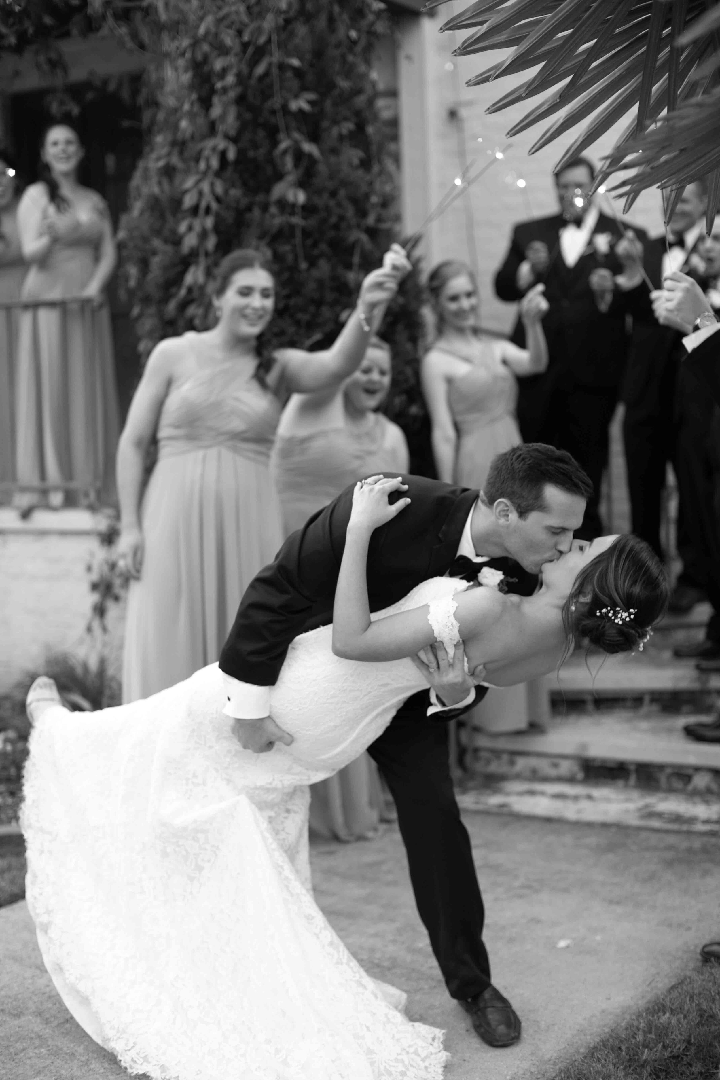 wedding party celebrates with sparkler send off as bride and groom kiss