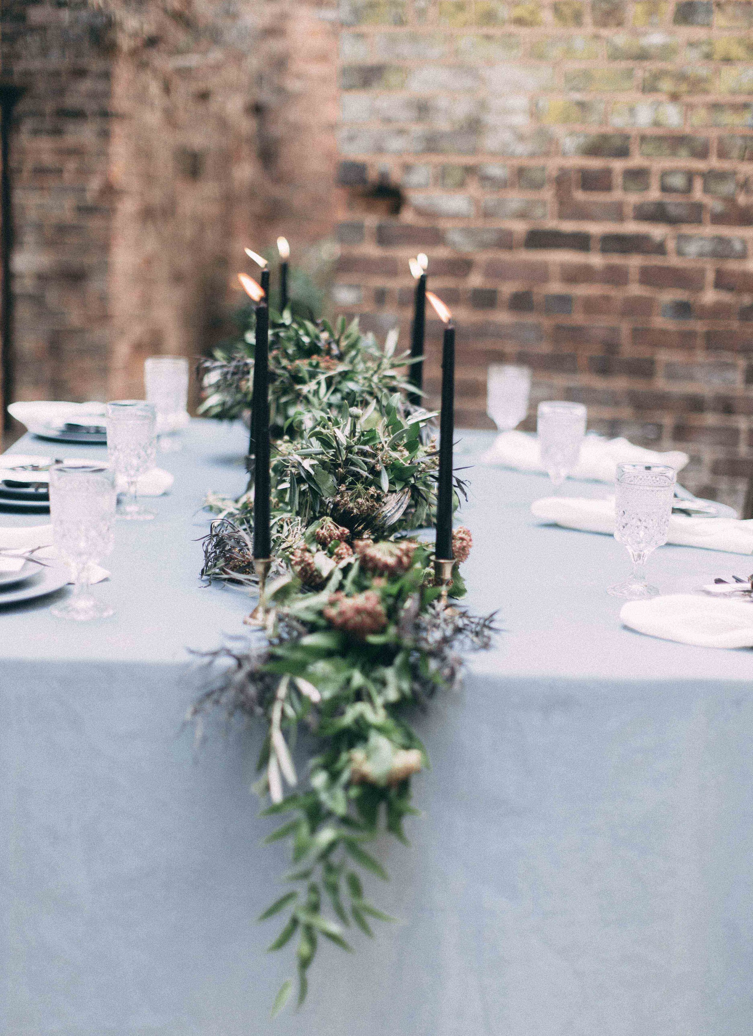Dusty blue table setting with black candles and natural greenery