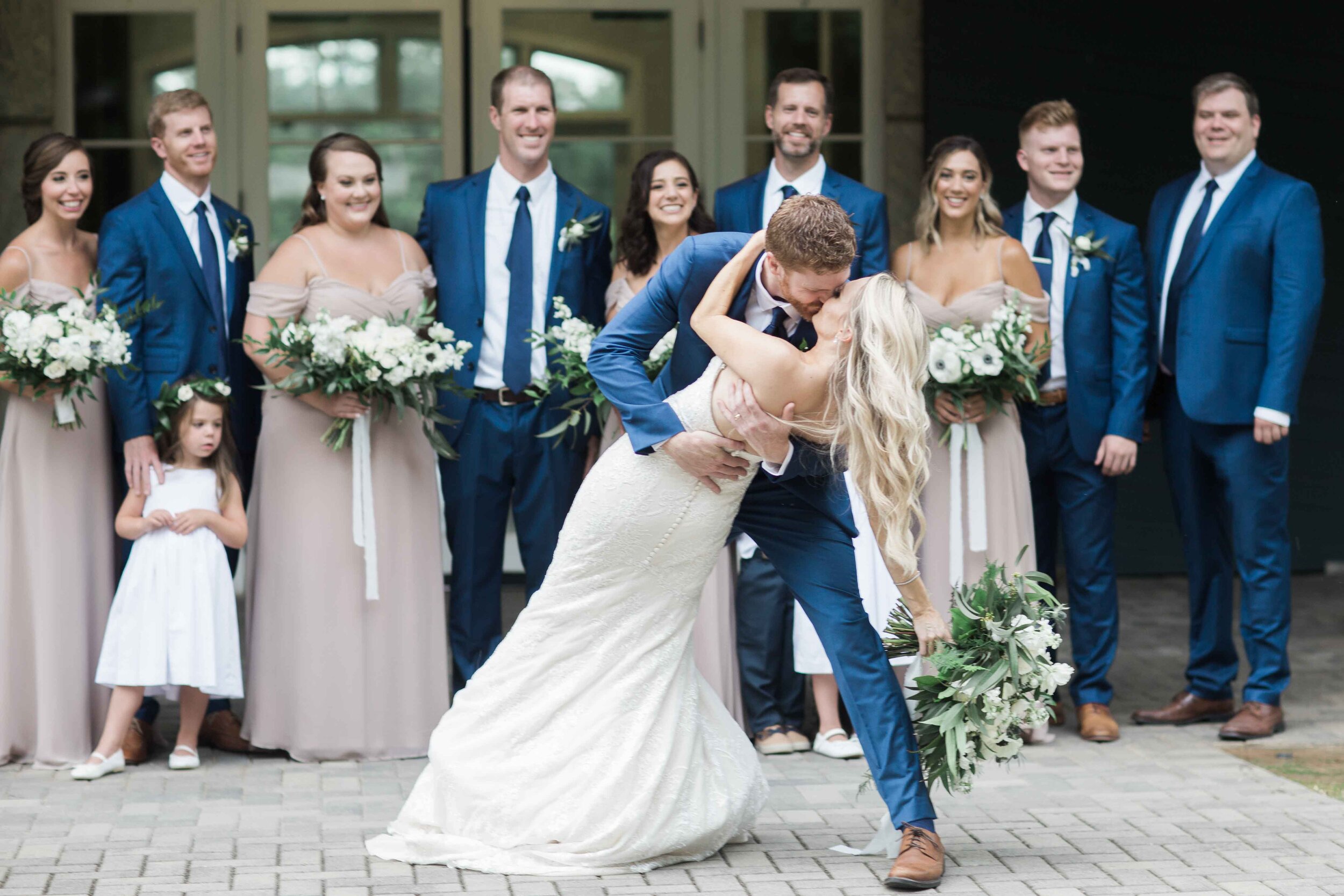 Blue suit groomsmen nude bridesmaids smiling bride and groom kiss 