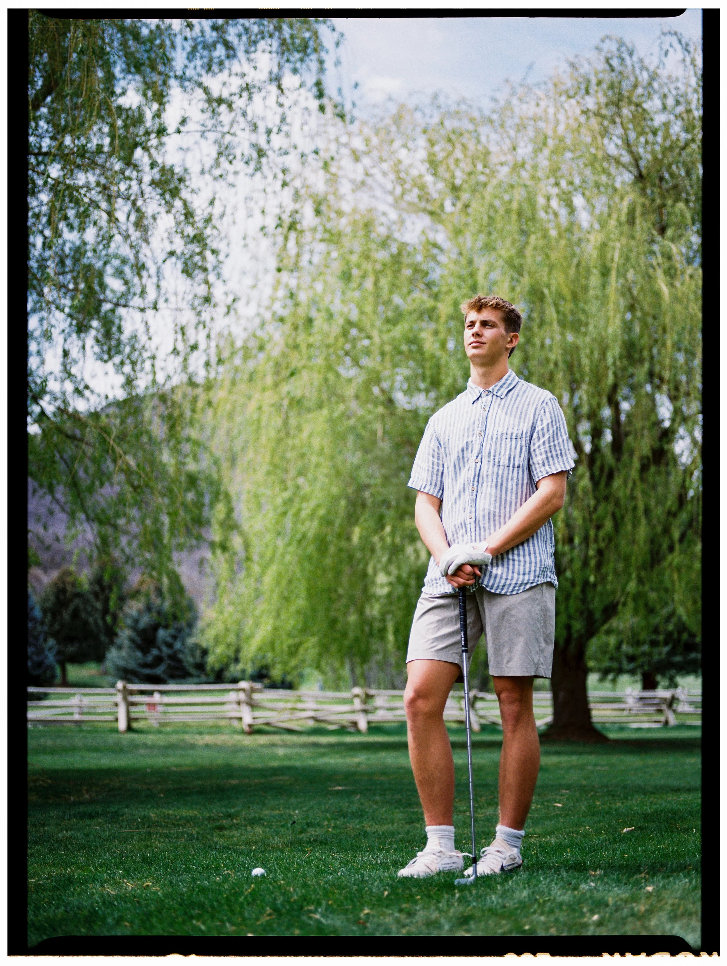 man poses with gold club on green with weeping willows