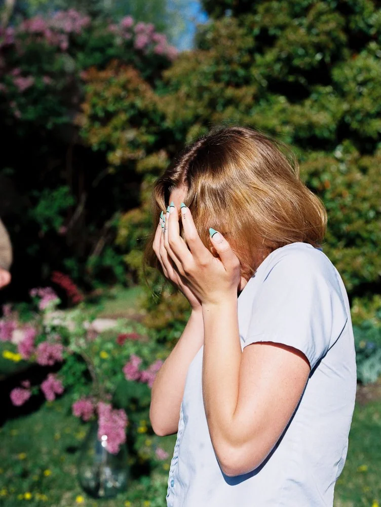 girl covers face blue shirt with lilacs and teal french manicure