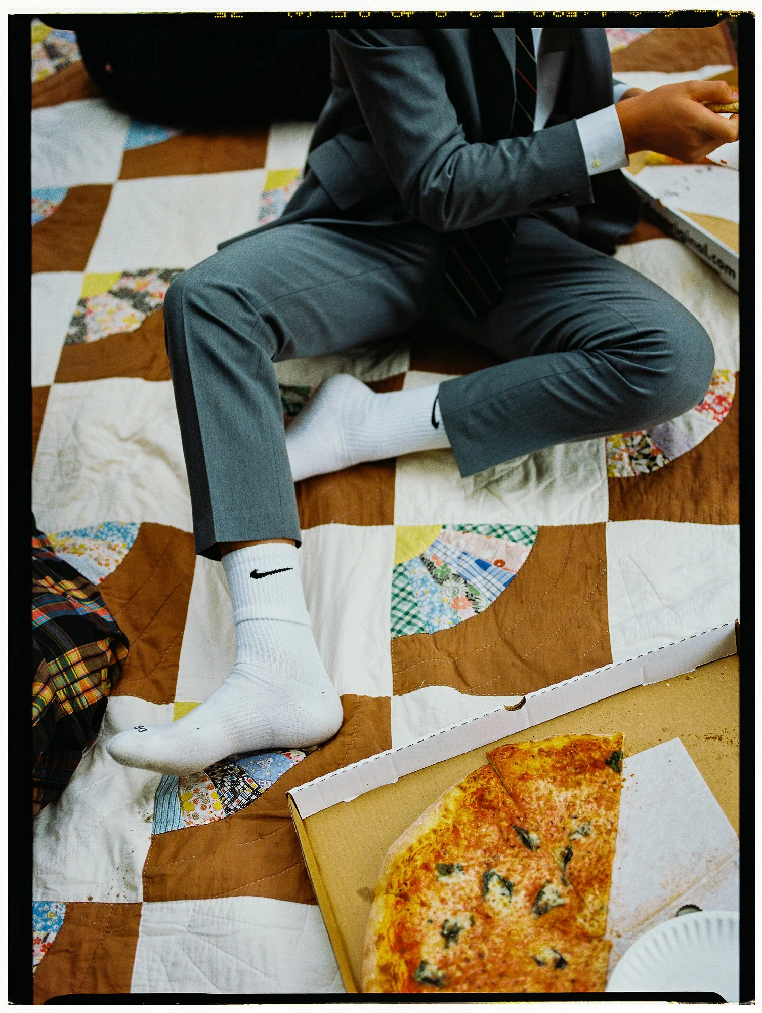 boy in suit and nike socks sits on antique quilt with pizza
